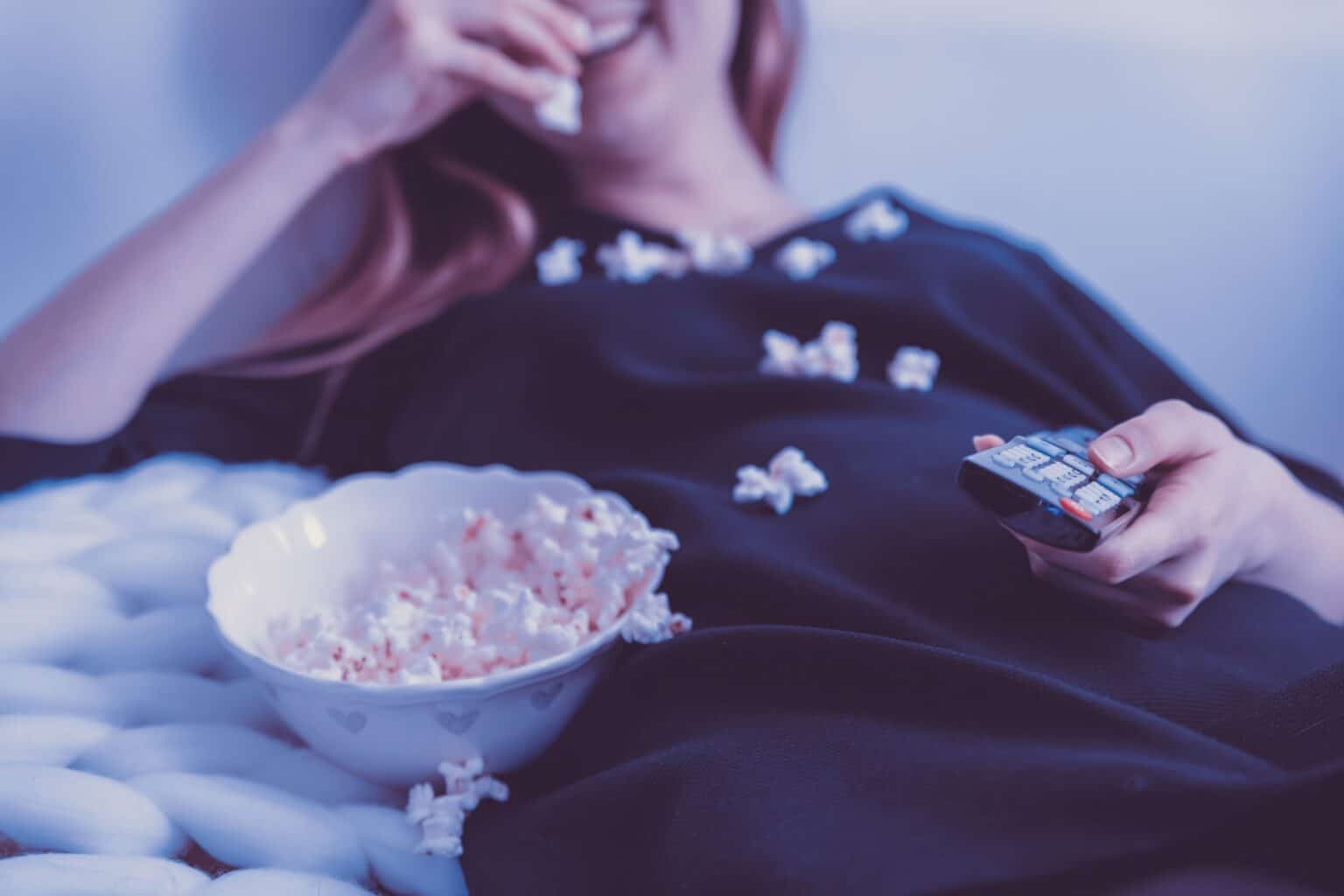A person relaxing with popcorn and a remote control, preparing for a cozy movie night at home.