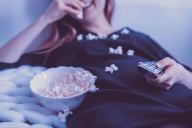 A person relaxing with popcorn and a remote control, preparing for a cozy movie night at home.