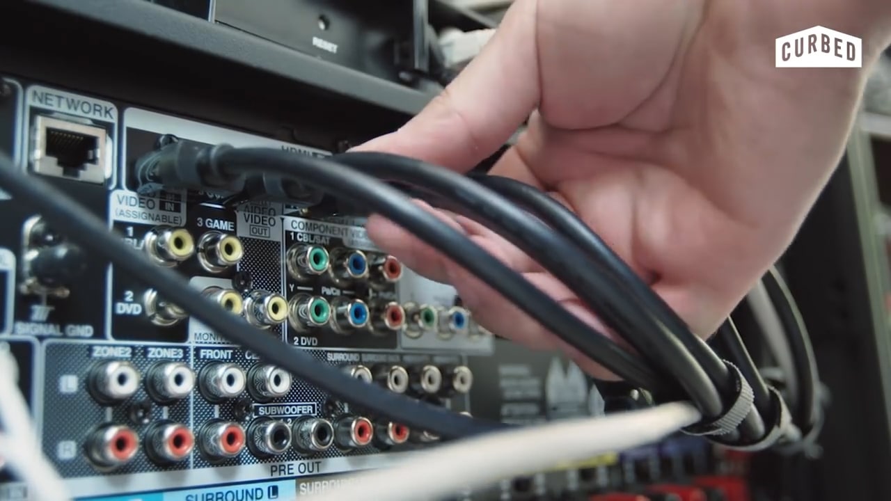 Close-up of a hand adjusting tangled cables on a mismanaged home theater receiver installation.