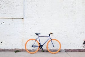 Minimalist bicycle with orange wheels against a white wall, symbolizing the rise of smart e-bikes as part of modern smart living.