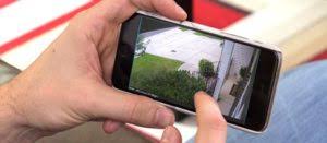 Close-up of a person monitoring their driveway through a smart security camera feed on a smartphone.