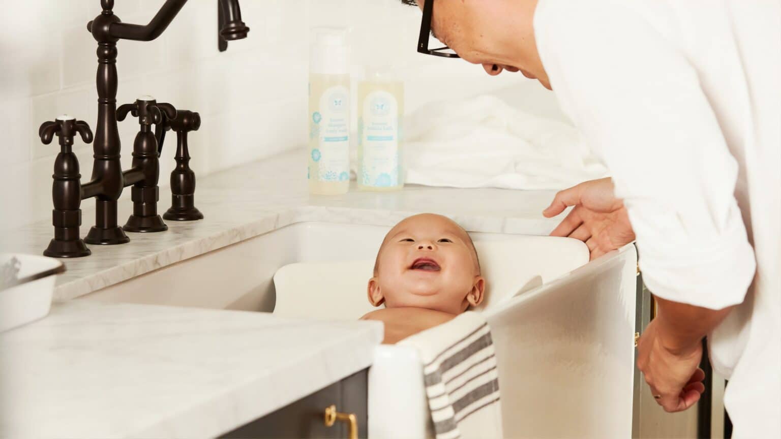 Parent bathing a smiling baby in a modern bathroom, highlighting comfort and relaxation.