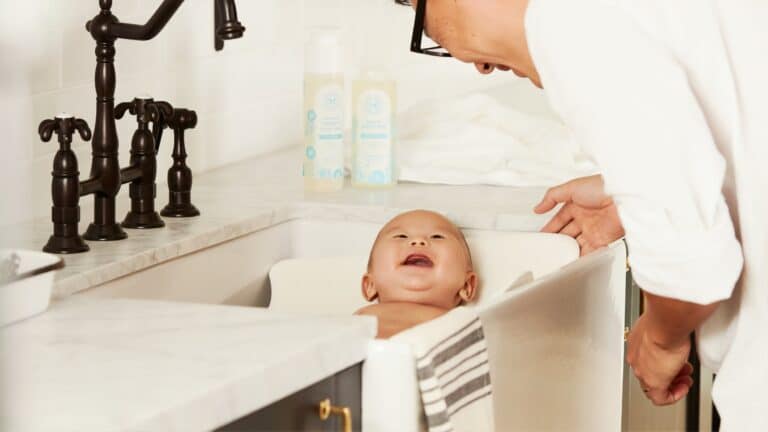 Parent bathing a smiling baby in a modern bathroom, highlighting comfort and relaxation.