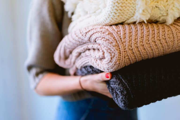 Person holding a stack of folded sweaters, symbolizing laundry done with smart home efficiency.