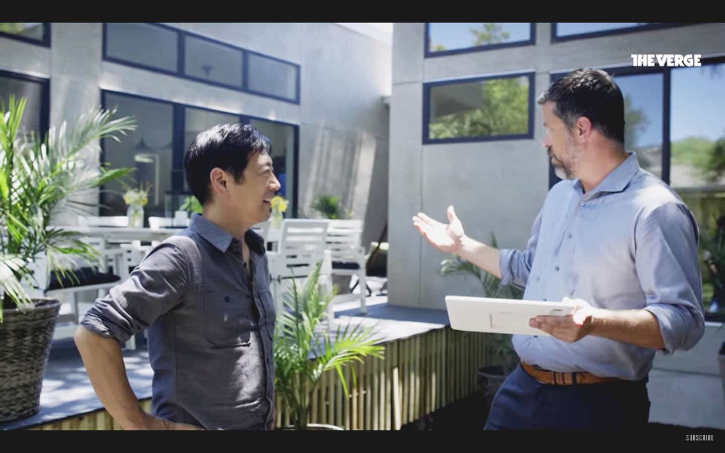 Two men discussing technology outdoors, one holding a tablet, representing troubleshooting with a smart home manager for better Wi-Fi coverage.