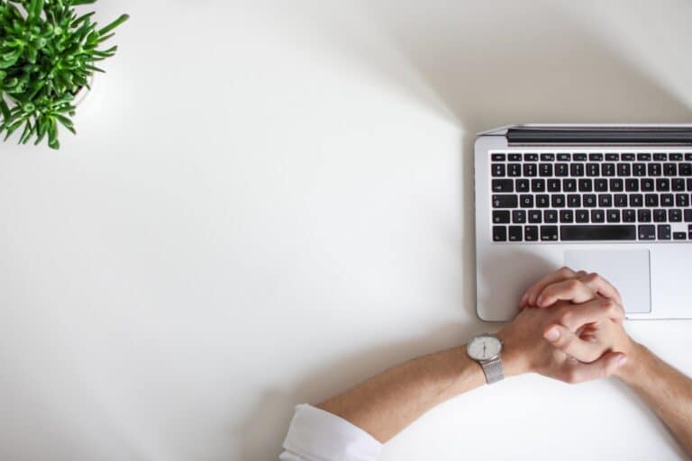Laptop on a desk with hands folded in frustration, symbolizing slow internet affecting smart home technology.