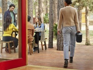 Person carrying a portable smart speaker outdoors toward friends, symbolizing gift ideas for home improvement enthusiasts and smart home devices.