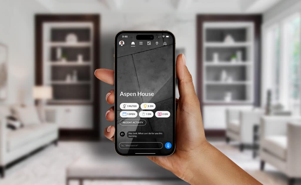 Hand holding a smartphone with a smart home interface controlling lighting and automation in a modern living room.
