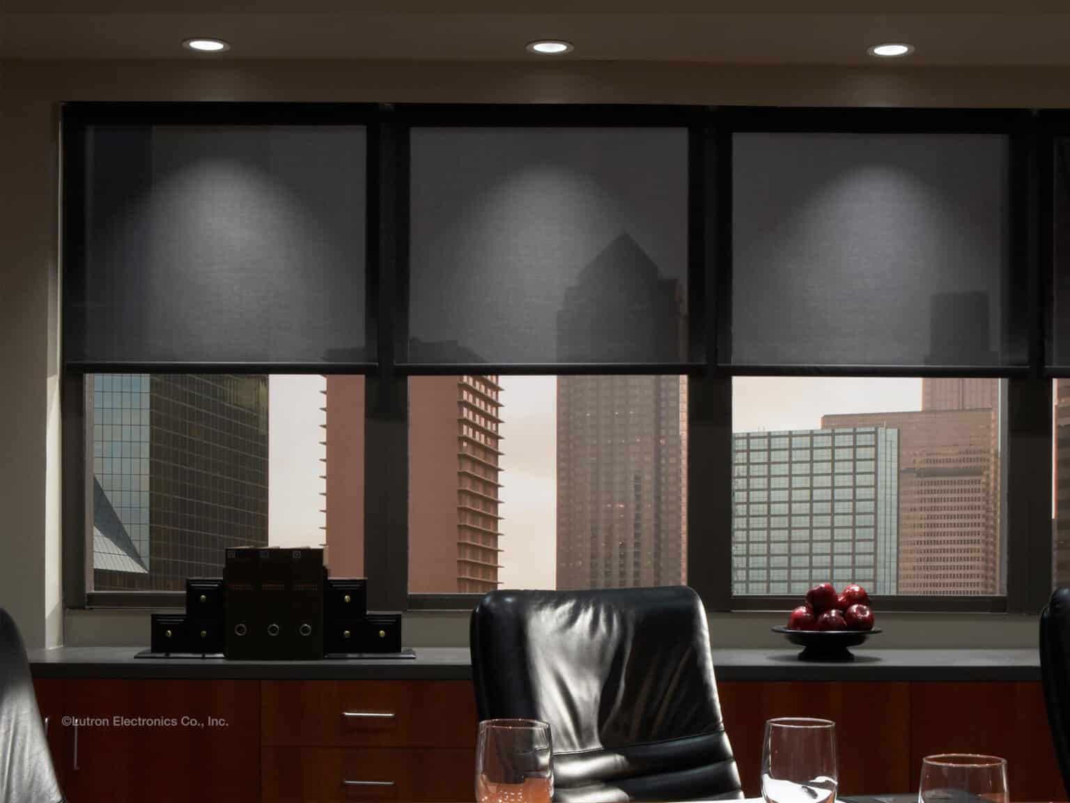 Office interior with motorized Lutron shades partially lowered, revealing a city skyline through the windows.