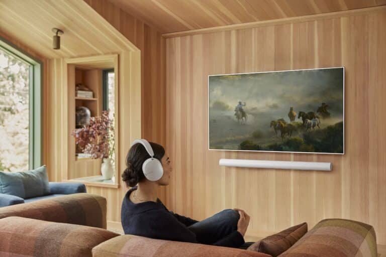 Person enjoying a movie with headphones in a cozy living room featuring a mounted TV and soundbar, representing a home theatre experience.