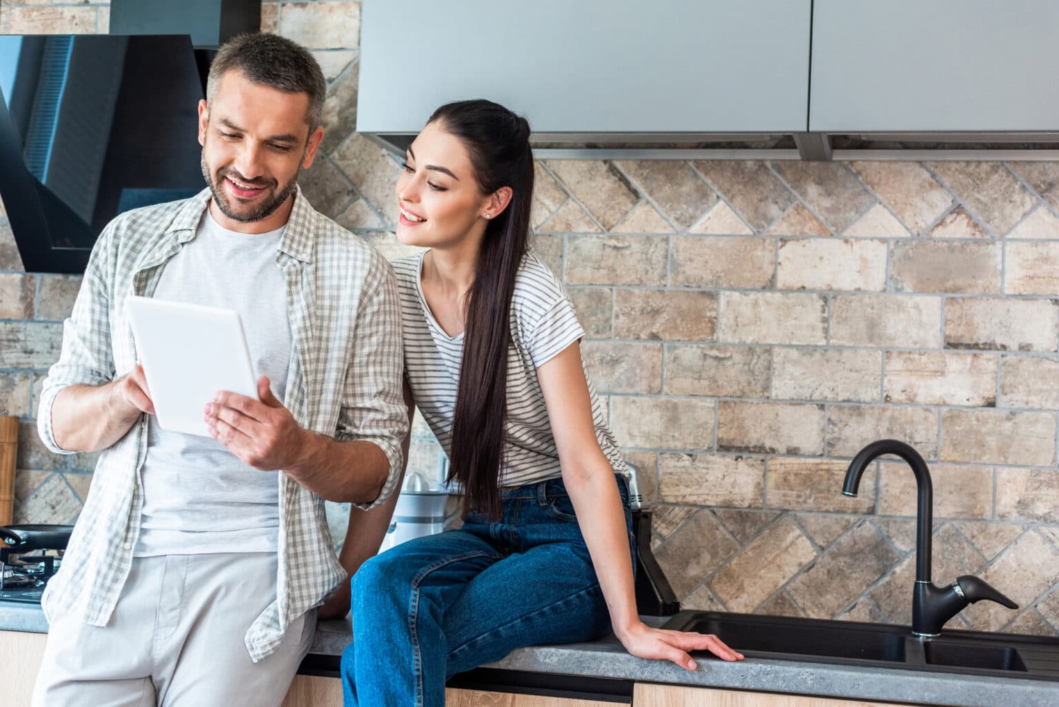 Couple in a modern kitchen using a tablet to manage their smart home devices.